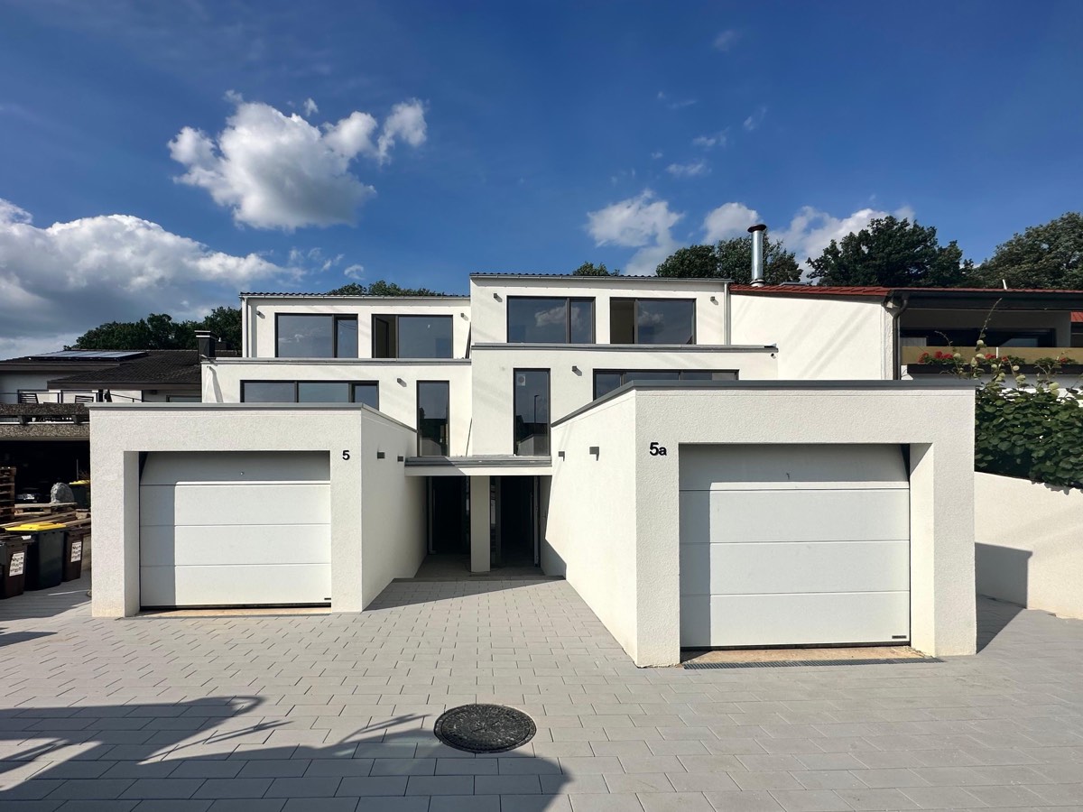 Fertiggestelltes Doppelhaus mit zwei weißen Garagen und gepflasterter Hoffläche