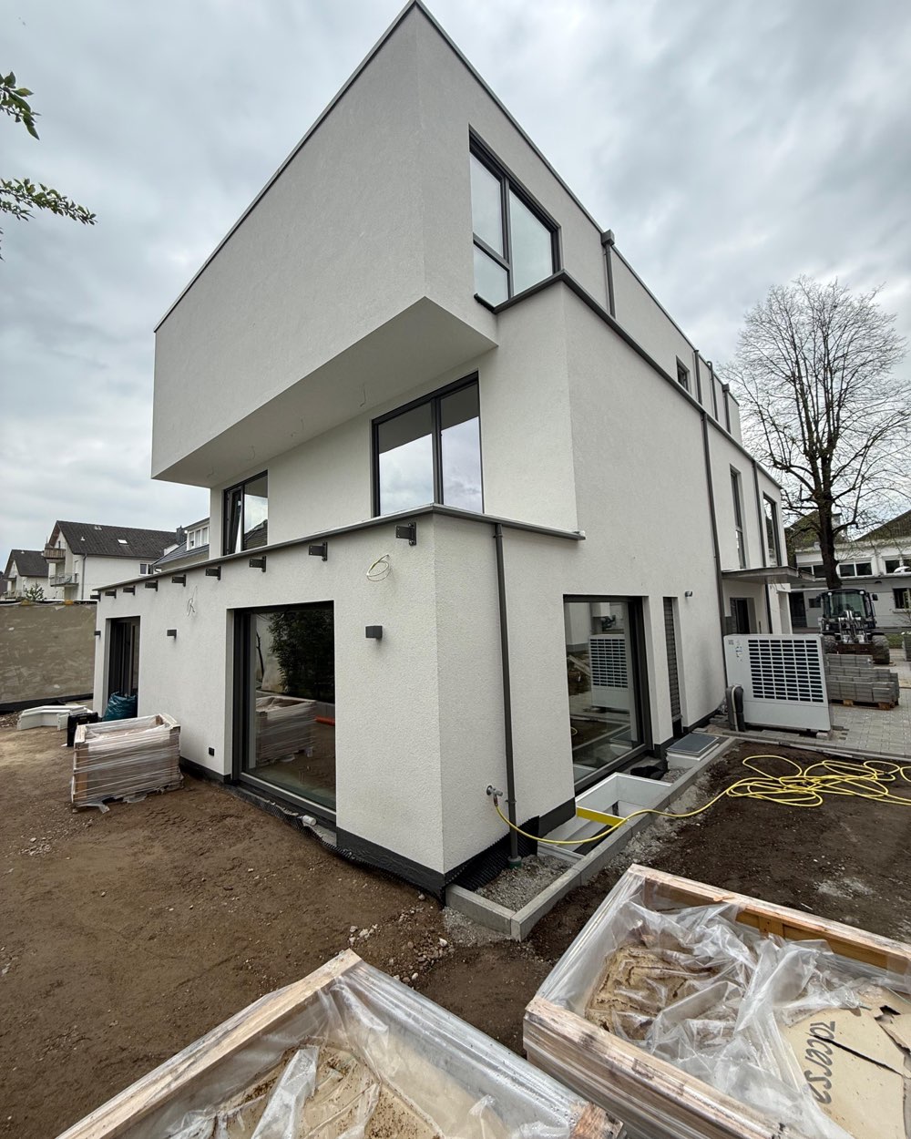 Neubau kurz vor der Fertigstellung: weiße Putzfassade und auskragendes Obergeschoss stehen, die Außenanlage ist noch Baustelle